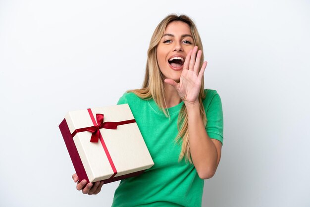 Young Uruguayan woman holding a gift isolated on white background shouting with mouth wide open
