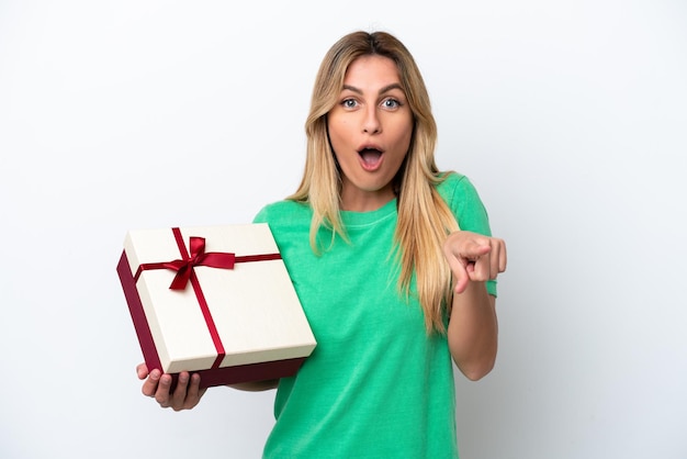 Young Uruguayan woman holding a gift isolated on white background surprised and pointing front