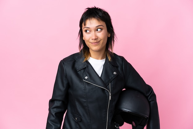 Young Uruguayan woman holding a motorcycle helmet over isolated pink background standing and looking to the side