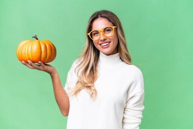 Young Uruguayan woman holding a pumpkin over isolated background smiling a lot