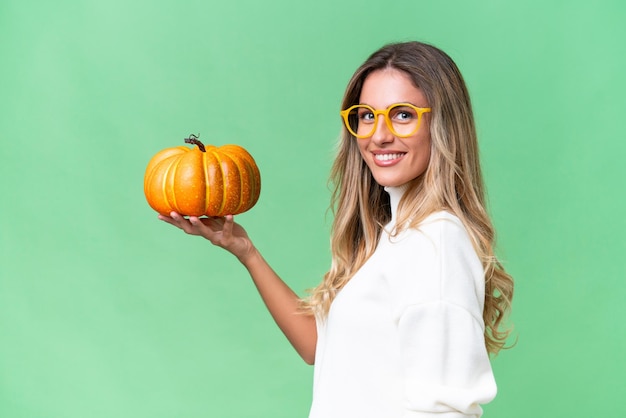 Young uruguayan woman holding a pumpkin over isolated background smiling a lot