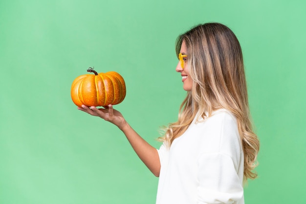 Young Uruguayan woman holding a pumpkin over isolated background with happy expression