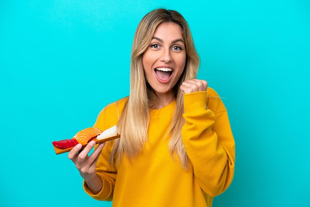 Young Uruguayan woman holding sashimi isolated on blue background celebrating a victory in winner position