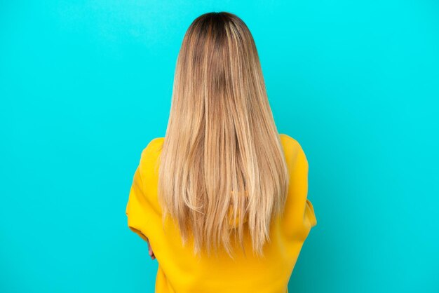 young uruguayan woman isolated on blue background in back position