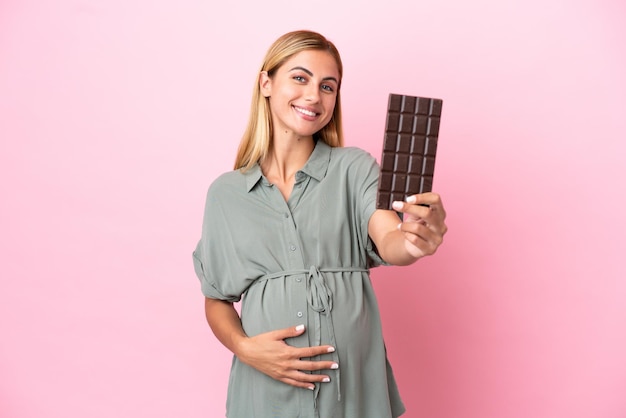 Young Uruguayan woman isolated on blue background pregnant and holding chocolate