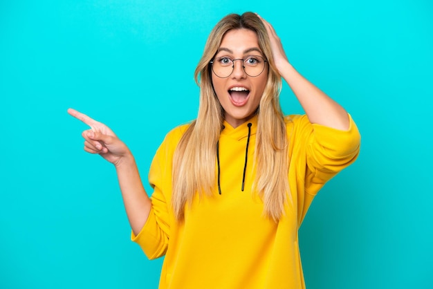 Young Uruguayan woman isolated on blue background surprised and pointing finger to the side