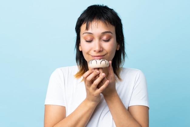 Young Uruguayan woman over isolated blue holding a donut