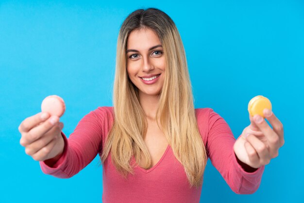 Giovane donna uruguaiana sopra la parete blu isolata che offre macarons francesi variopinti