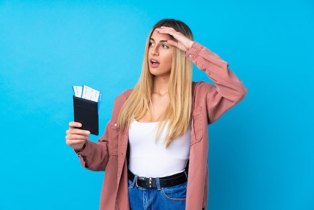 Foto giovane donna uruguaiana sopra la parete blu isolata della parete in vacanza con il passaporto e i biglietti aerei mentre guardando qualcosa nella distanza