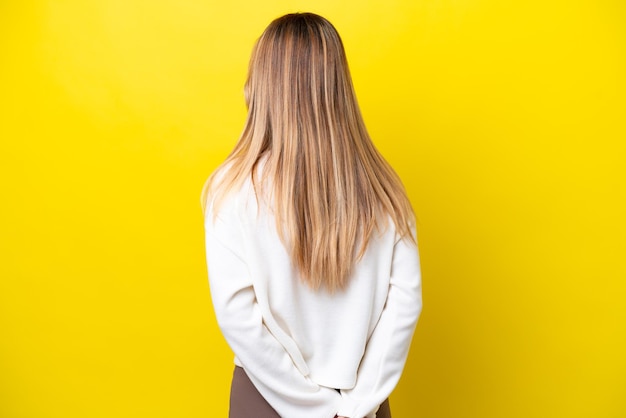 Young uruguayan woman isolated on yellow background in back position and looking back