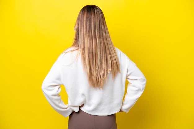 young uruguayan woman isolated on yellow background in back position