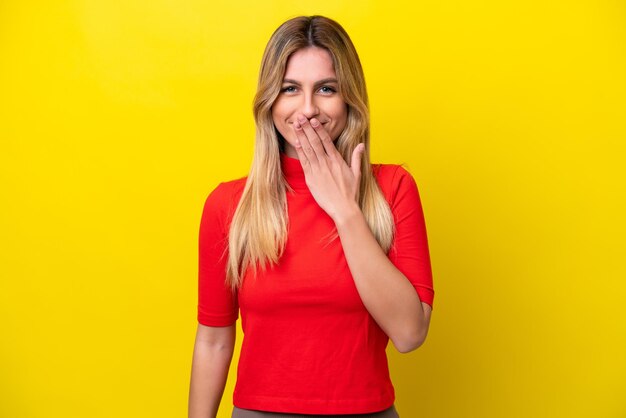 Giovane donna uruguaiana isolata su sfondo giallo felice e sorridente che copre la bocca con la mano