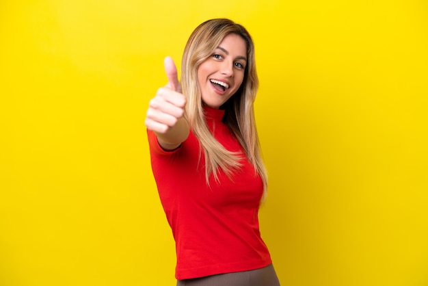 Young Uruguayan woman isolated on yellow background with thumbs up because something good has happened