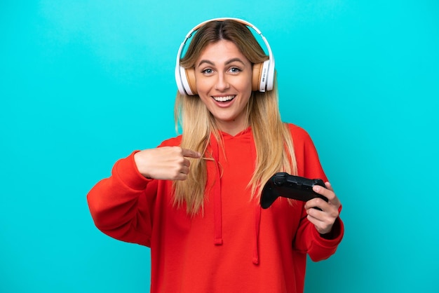 Young Uruguayan woman playing with a video game controller isolated on blue with surprise facial expression