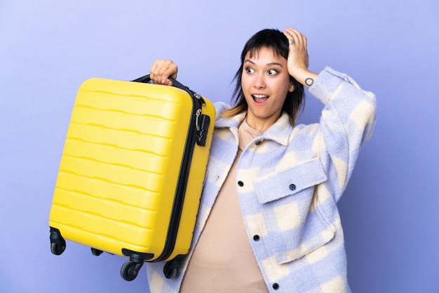 Young Uruguayan woman over purple wall in vacation with travel suitcase and surprised