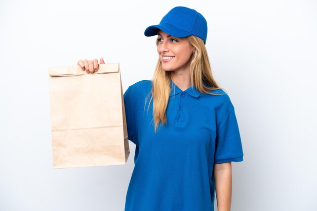 Young Uruguayan woman taking a bag of takeaway food isolated on white background looking to the side and smiling