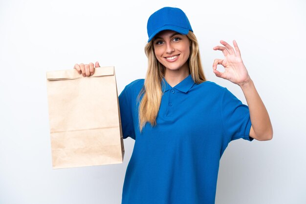 Young Uruguayan woman taking a bag of takeaway food isolated on white background showing ok sign with fingers