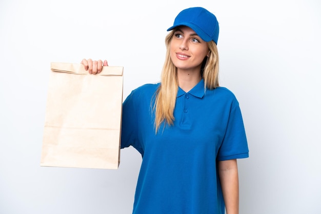 Young Uruguayan woman taking a bag of takeaway food isolated on white background thinking an idea while looking up