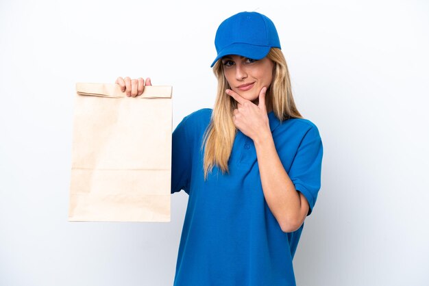 Young Uruguayan woman taking a bag of takeaway food isolated on white background thinking