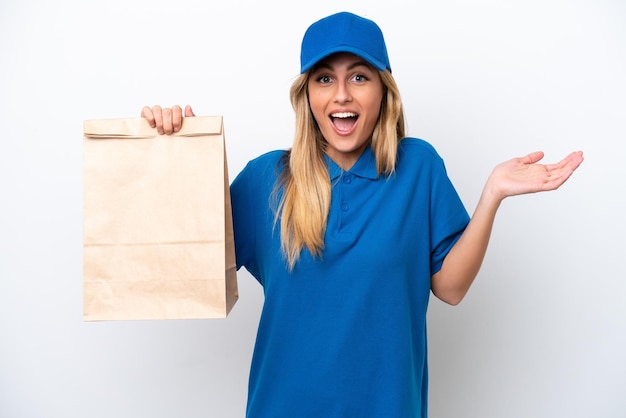 Young Uruguayan woman taking a bag of takeaway food isolated on white background with shocked facial expression