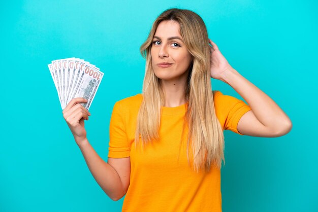 Young Uruguayan woman taking a lot of money isolated on blue background having doubts