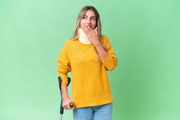 Young Uruguayan woman wearing neck brace and crutches over isolated background with surprise and shocked facial expression