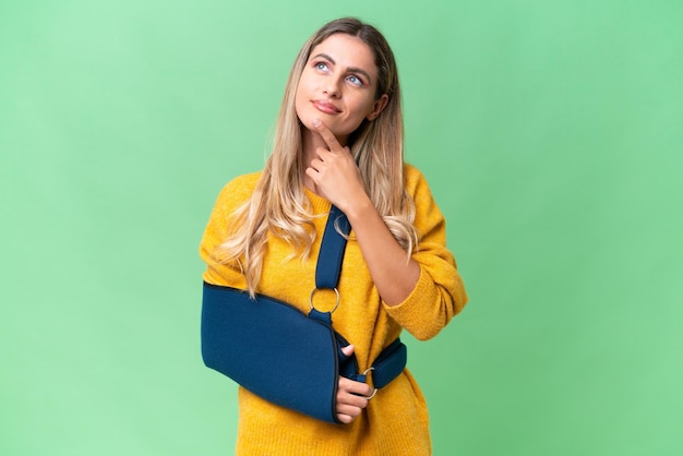 Young Uruguayan woman with broken arm and wearing a sling over isolated background having doubts