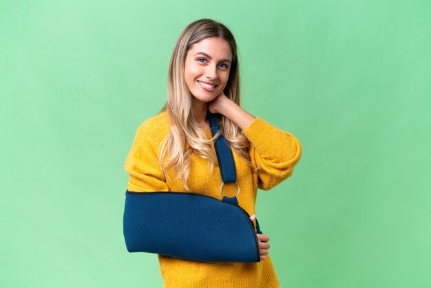 Young Uruguayan woman with broken arm and wearing a sling over isolated background laughing