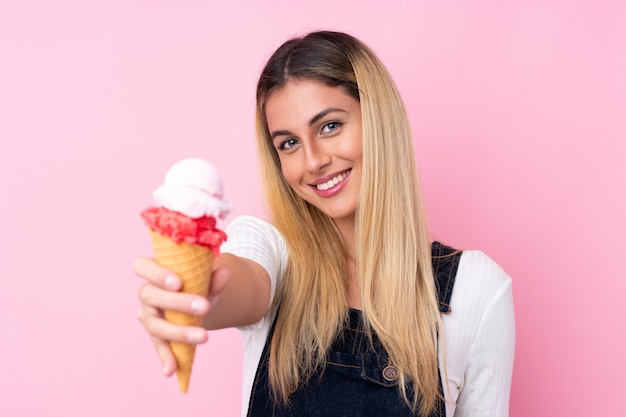 Young Uruguayan woman with a cornet ice cream over isolated pink wall