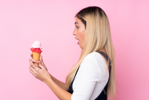 Young Uruguayan woman with a cornet ice cream over isolated pink wall