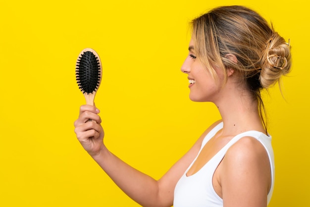 Photo young uruguayan woman with hair comb isolated on yellow background with happy expression