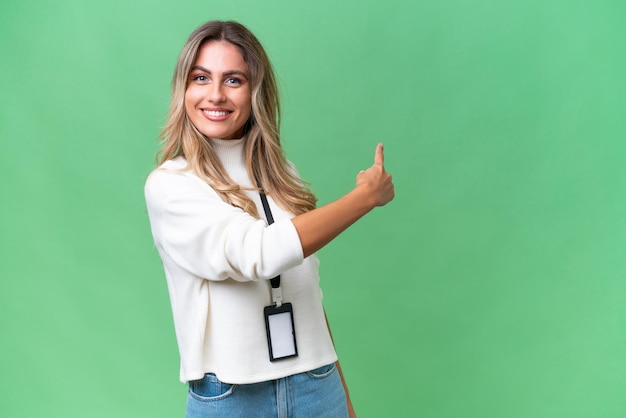 Young Uruguayan woman with ID card over isolated background pointing back