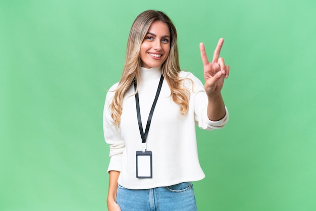 Young Uruguayan woman with ID card over isolated background smiling and showing victory sign