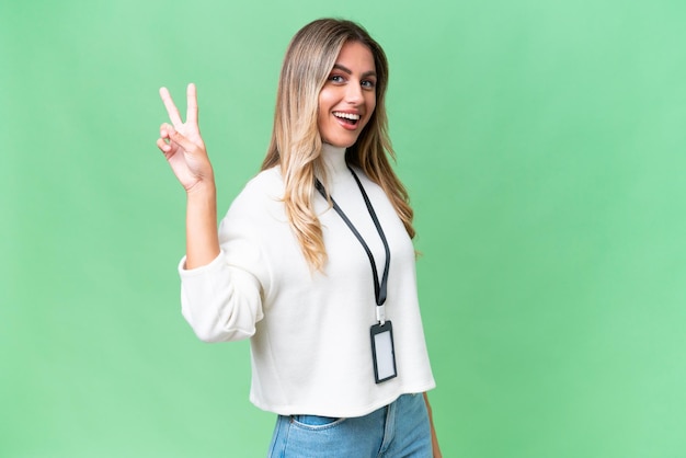 Young Uruguayan woman with ID card over isolated background smiling and showing victory sign