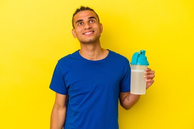 Young venezuelan man drinking a protein shake isolated on yellow background dreaming of achieving goals and purposes