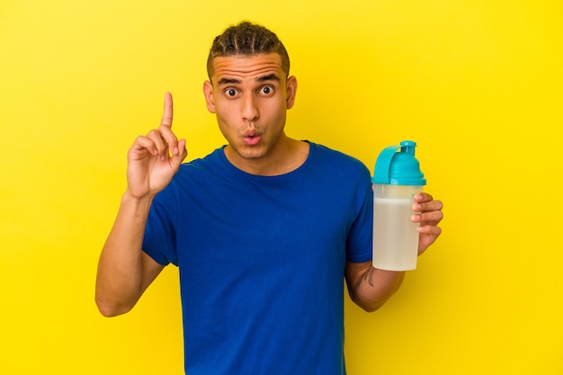 Young venezuelan man drinking a protein shake isolated on yellow background having an idea, inspiration concept.