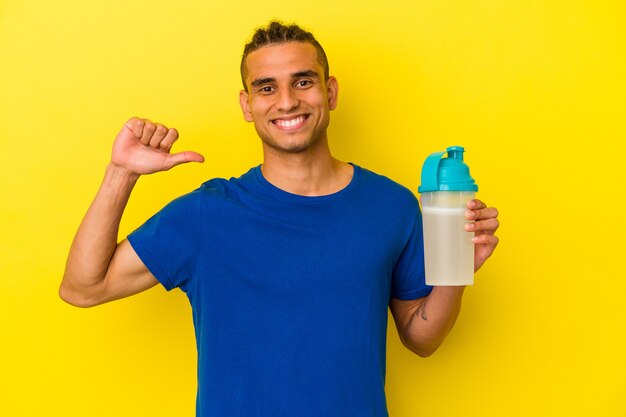Young venezuelan man drinking a protein shake isolated on yellow wall feels proud and self confident, example to follow.