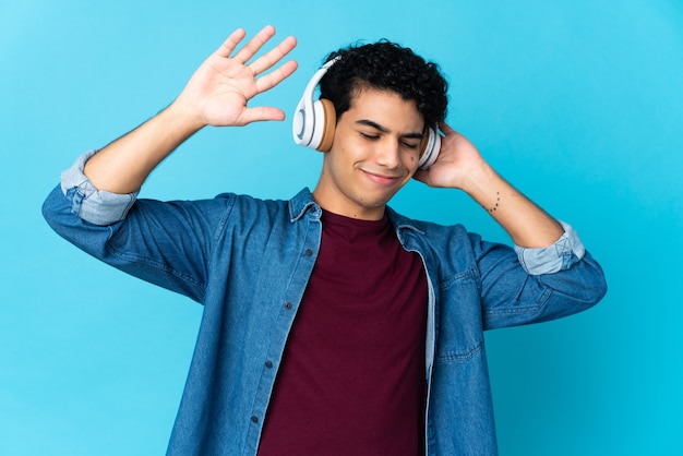 Young Venezuelan man isolated on blue listening music and dancing