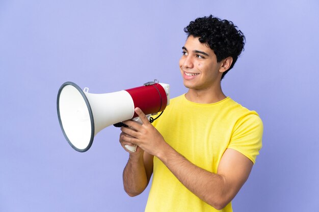 Young Venezuelan man isolated on purple wall shouting through a megaphone to announce something