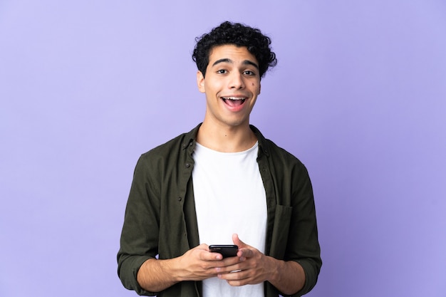 Young Venezuelan man isolated on purple wall surprised and sending a message