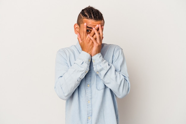Young venezuelan man isolated on white background blink through fingers frightened and nervous.