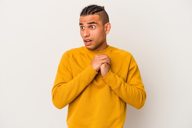 Young venezuelan man isolated on white background praying for luck, amazed and opening mouth looking to front.