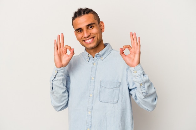 Young venezuelan man isolated on white wall cheerful and confident showing ok gesture.