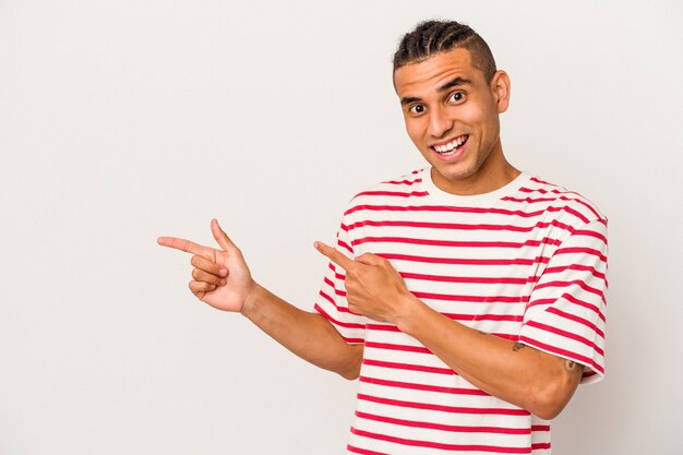 Young venezuelan man isolated on white wall excited pointing with forefingers away.