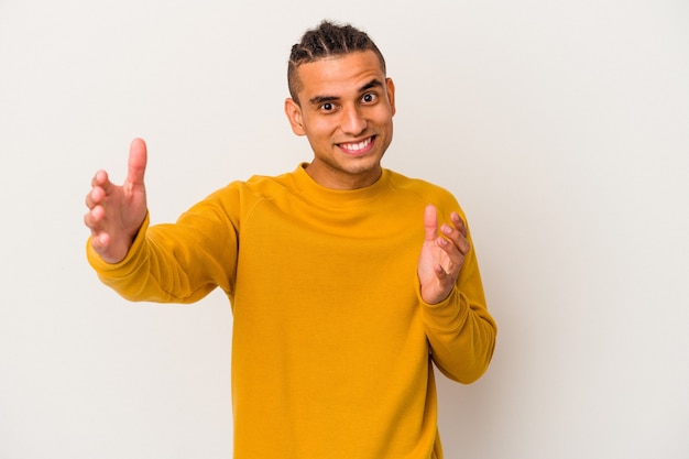 Young venezuelan man isolated on white wall feels confident giving a hug to you