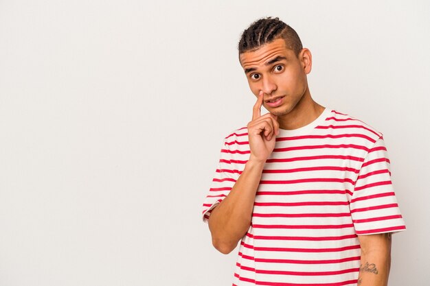 Young venezuelan man isolated on white wall looking sideways with doubtful and skeptical expression.