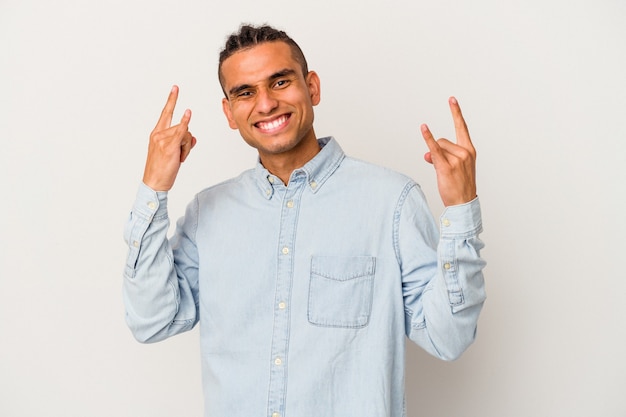 Young venezuelan man isolated on white wall showing a horns gesture as a revolution concept.