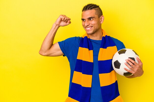 Young venezuelan man watching soccer isolated on yellow wall raising fist after a victory, winner concept