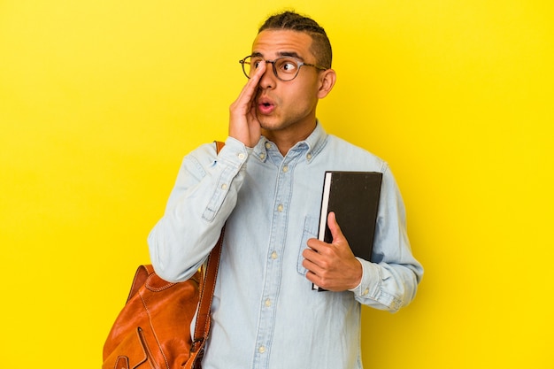 Young venezuelan student man isolated on yellow wall shouting and holding palm near opened mouth