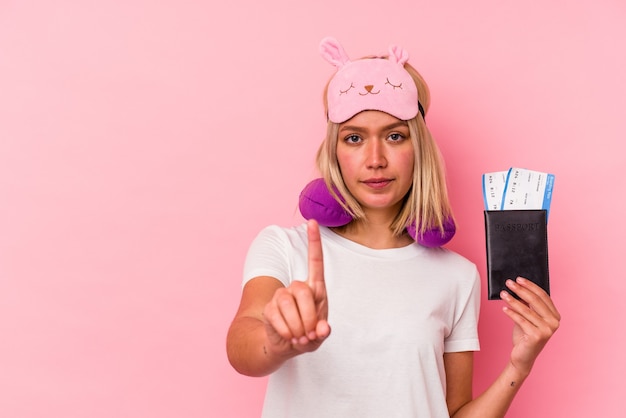 Photo young venezuelan traveler woman holding a passport isolated on pink background showing number one with finger.